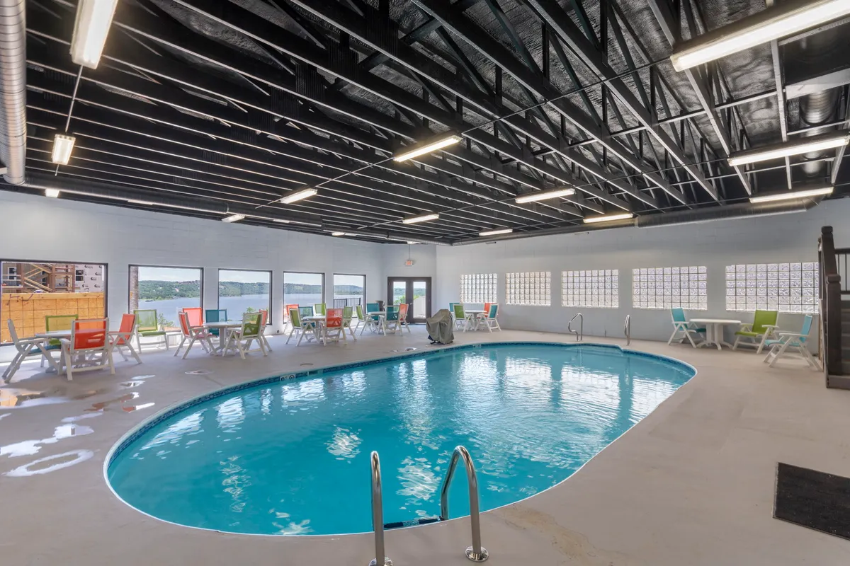 A bright, cheerful indoor swimming pool area featuring colorful lounge chairs and expansive windows that let in natural light. The space looks welcoming and is ideal for both relaxation and social gatherings, capturing the all-weather, year-round aspect of resort-style amenities.