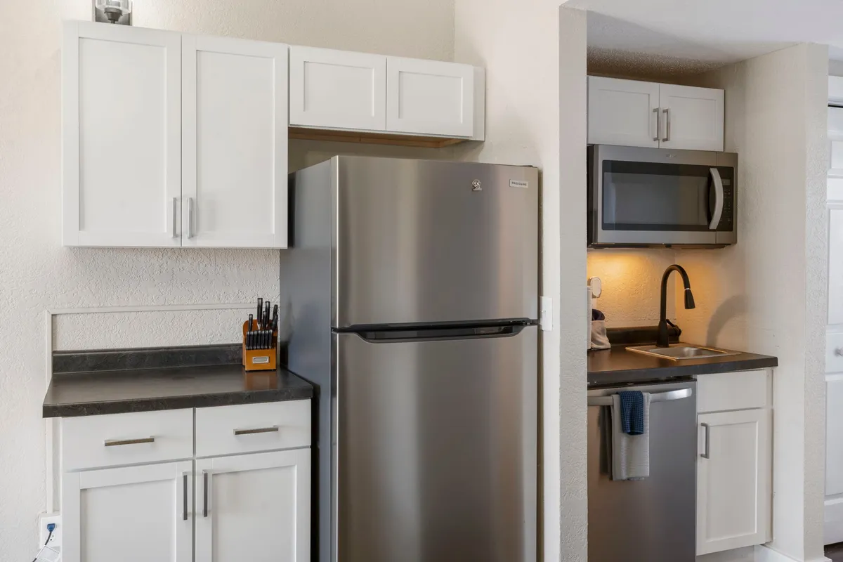 A functional, streamlined kitchen space featuring a stainless steel refrigerator, modern cabinetry, a kitchen sink, and a microwave. The image conveys a sense of readiness for meal prep and group gatherings, with modern finishes that enhance the overall appeal.