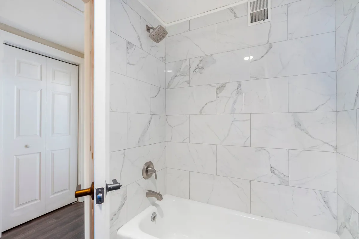 A modern bathroom featuring a sleek bathtub, marble tiles, and a convenient showerhead. The space feels clean, serene, and ideal for a refreshing soak or an energizing shower after a long day.