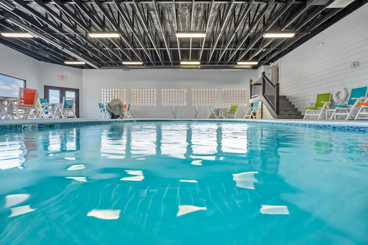 A bright indoor swimming pool with colorful lounge chairs, an inviting pool, and a staircase leading up to another level. The space feels fresh and lively, perfect for cooling off or unwinding with friends after a day of activities.