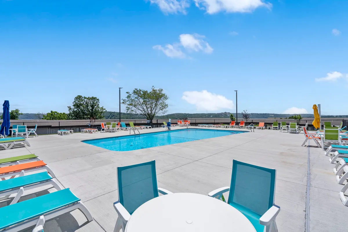 A beautifully landscaped outdoor swimming pool surrounded by colorful lounge chairs under a clear blue sky. The setting is vibrant, with space for sunbathing, socializing, and enjoying leisurely swims, reinforcing the seasonal outdoor pool experience.