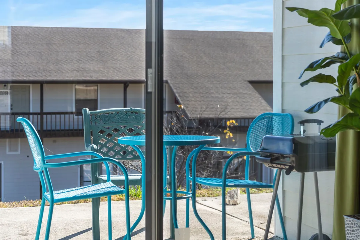 A cheerful exterior patio setup with blue furniture, a small grill, and a green plant, designed for outdoor dining and unwinding. The patio space is intimate, ideal for sipping coffee or grilling at sunset.