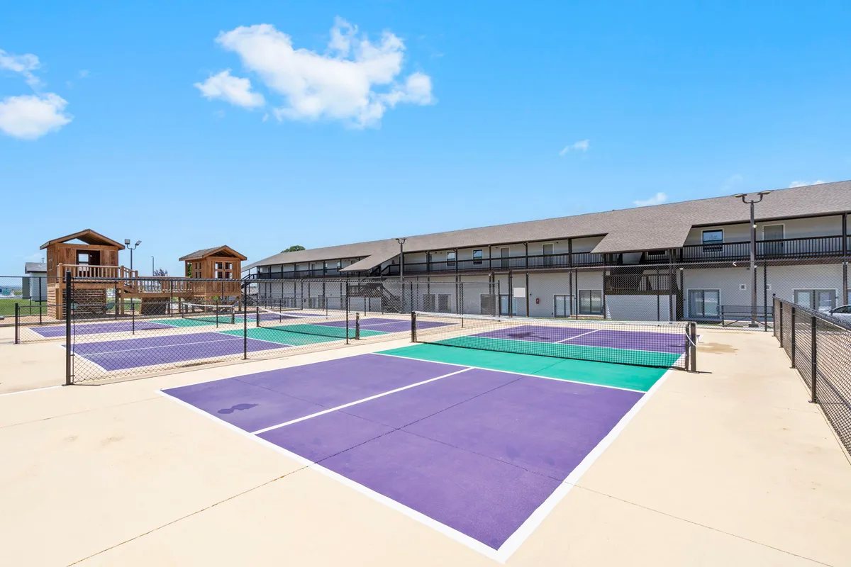 A lively exterior scene featuring tennis courts and a modern playground structure, nestled within greenery. Children are seen playing while adults enjoy tennis, reflecting the diverse, multigenerational activities available for guests.